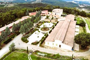 Vue aérienne d’une propriété comprenant un grand bâtiment central, une cour avec un jardin circulaire et des bâtiments annexes.