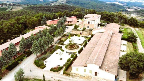 An aerial view of a property with a large central building, a courtyard with a circular garden, and surrounding structures.
