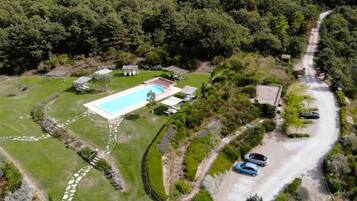 An aerial view of a property with a swimming pool, multiple small buildings, and a winding road.