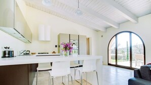 A modern kitchen with a white countertop, bar stools, and a large window.