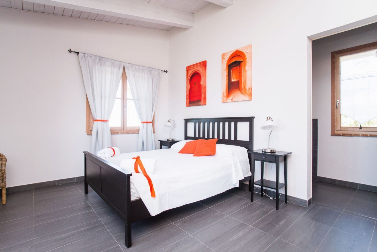 Une chambre à coucher bien rangée, avec un lit, des tables de chevet et une fenêtre avec des rideaux.