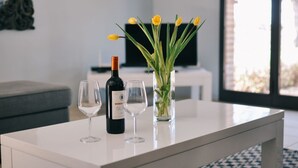 Ein modernes Wohnzimmer mit einem weißen Couchtisch, einer Weinflasche, zwei Weingläsern und einer Vase mit gelben Tulpen.