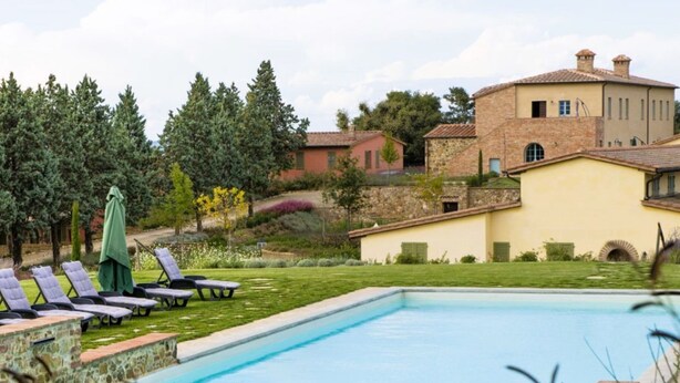 Ein Swimmingpool mit Liegestühlen und einem grünen Sonnenschirm, umgeben von einem Garten und einem Steinhaus.