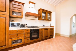 Een keuken met houten kastjes, een magnetron, fornuis, oven en een raam met uitzicht.