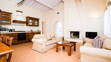 A spacious living area with a fireplace, a sofa, a coffee table, and a kitchen area with wooden cabinets and a tiled floor.