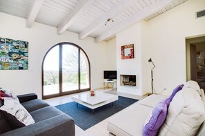 Un salon moderne doté d’une grande fenêtre en arc de cercle, d’un téléviseur à écran plat, d’une cheminée et d’un coin salon confortable.