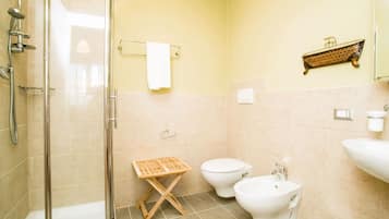 A bathroom with a glass shower enclosure, two toilets, a bidet, a sink, and a towel rack.