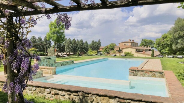 Une piscine rectangulaire bordée de pierres, entourée d’une pelouse et d’arbres.