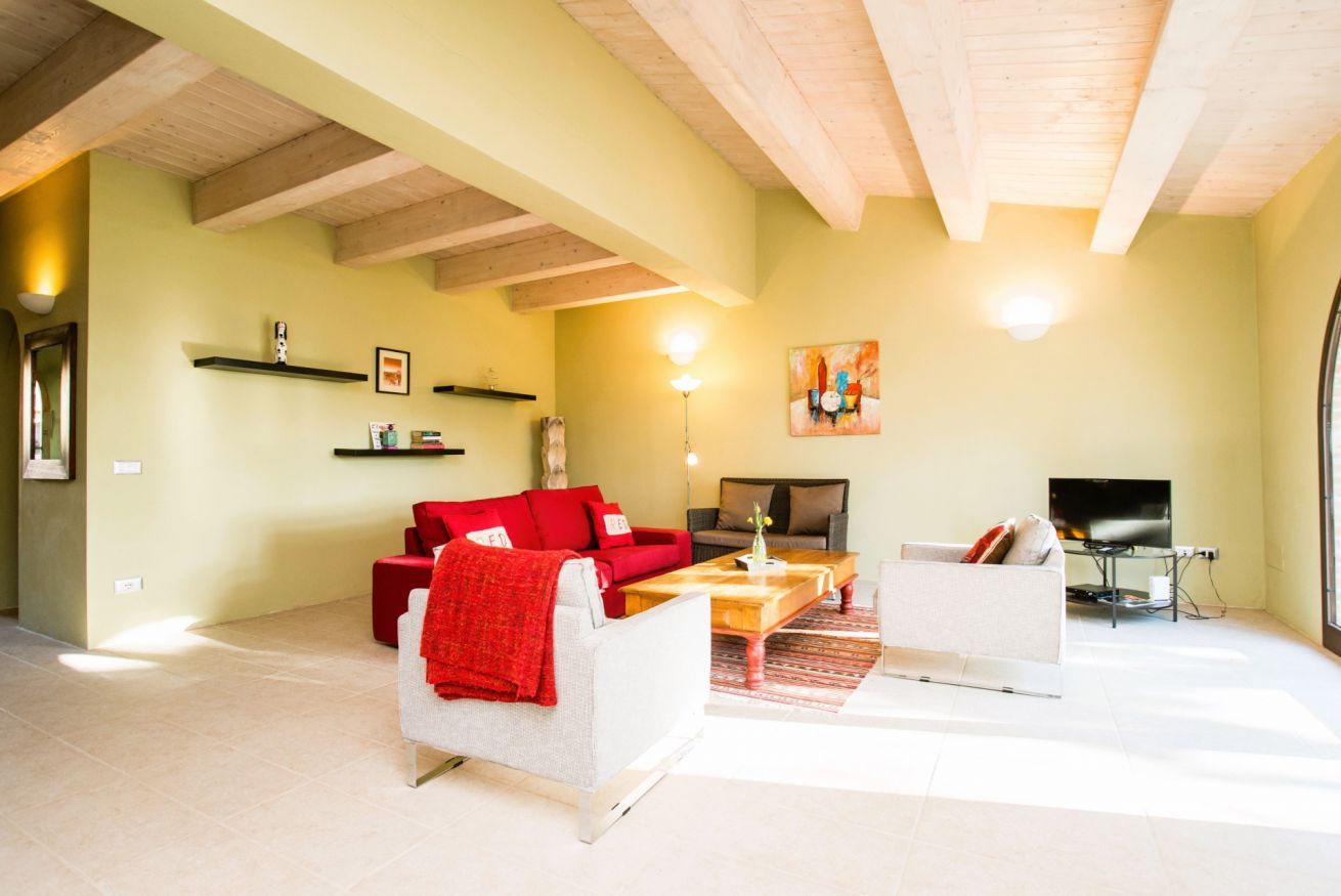 A living room with a red sofa, white armchair, and a coffee table. There is a TV and a fireplace.