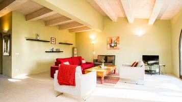 A living room with a red sofa, white armchair, and a coffee table. There is a TV and a fireplace.