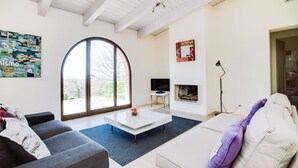 Un salon moderne doté d’une grande fenêtre en arc de cercle, d’un téléviseur à écran plat, d’une cheminée et d’un coin salon confortable.