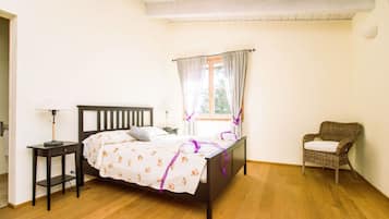 A bedroom with a wooden bed, a nightstand, a chair, and a window with curtains.
