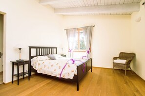 Ein Schlafzimmer mit einem hölzernen Bett, einem Nachttisch, einem Sessel und einem Fenster mit Vorhängen.