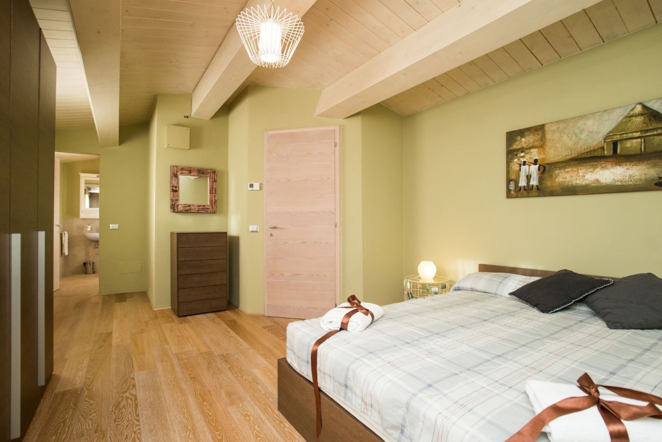 Une chambre à coucher avec un lit, un plancher en bois, une porte, un miroir et un tableau accroché au mur.