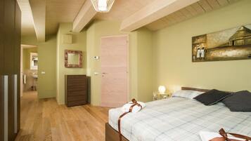 Une chambre à coucher avec un lit, un plancher en bois, une porte, un miroir et un tableau accroché au mur.