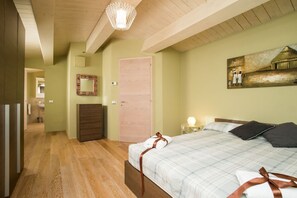 Ein Schlafzimmer mit einem Bett, Holzboden, einer Tür, einem Spiegel und einem Bild an der Wand.