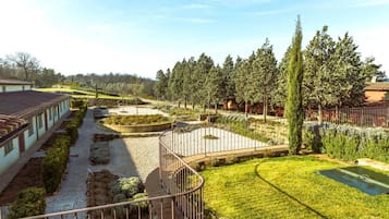 A courtyard with a pathway leading to a circular garden area, surrounded by trees and a building with a tiled roof.