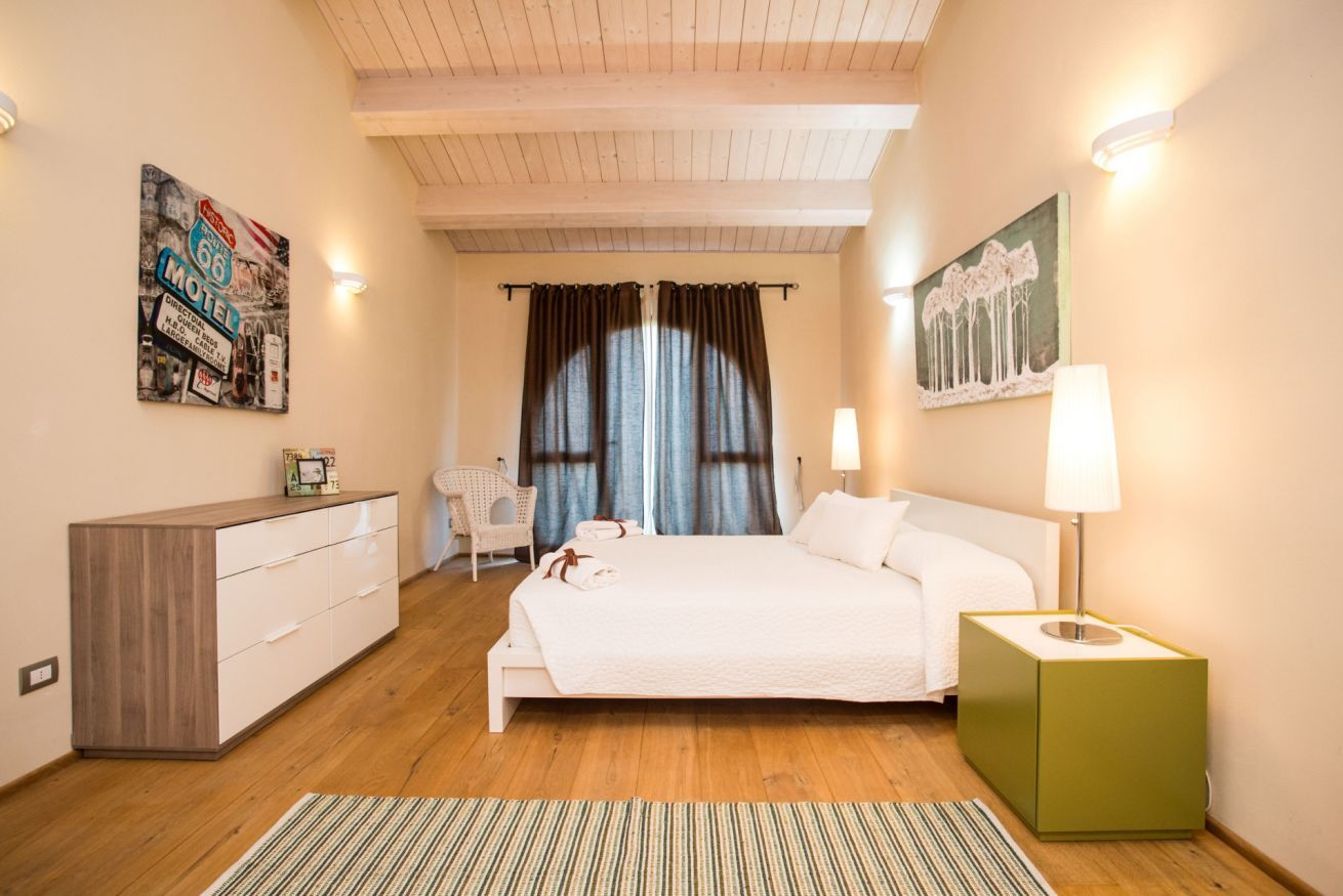 A bedroom with a bed, bedside table, dresser, and artwork on the walls.