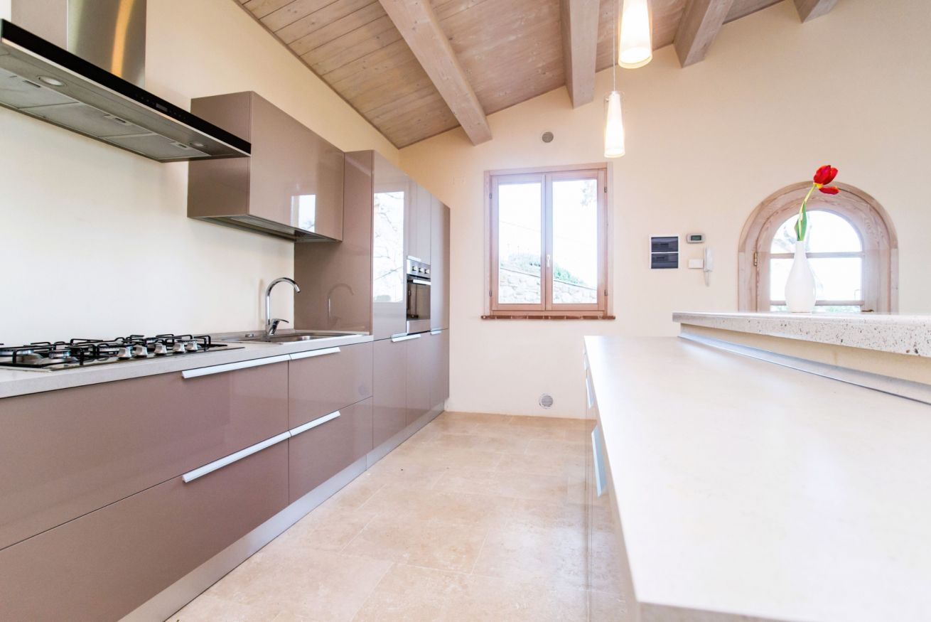 A modern kitchen with stainless steel appliances, wooden beams on the ceiling, and a window with a view.