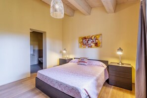 A bedroom with a bed, bedside tables, a hanging light fixture, and a painting on the wall.