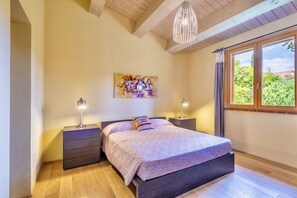 Een slaapkamer met een bed, twee nachtkastjes, een hanglamp, een raam met gordijnen en een schilderij aan de muur.