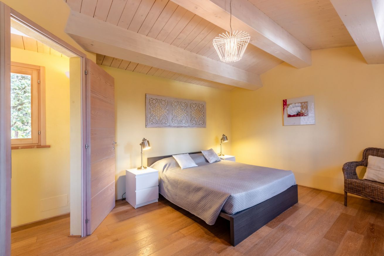 Une chambre à coucher comprenant un lit, des tables de chevet, une œuvre d’art murale et un luminaire suspendu.