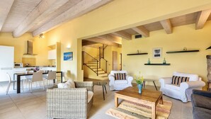 A spacious living area with a dining table, wicker furniture, and a staircase leading to an upper floor.