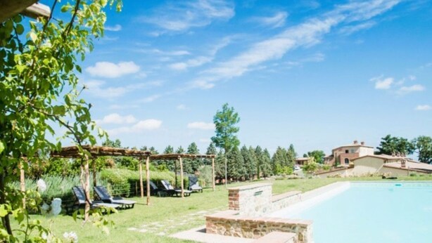 A pool area with a pergola, lounge chairs, and a stone structure.