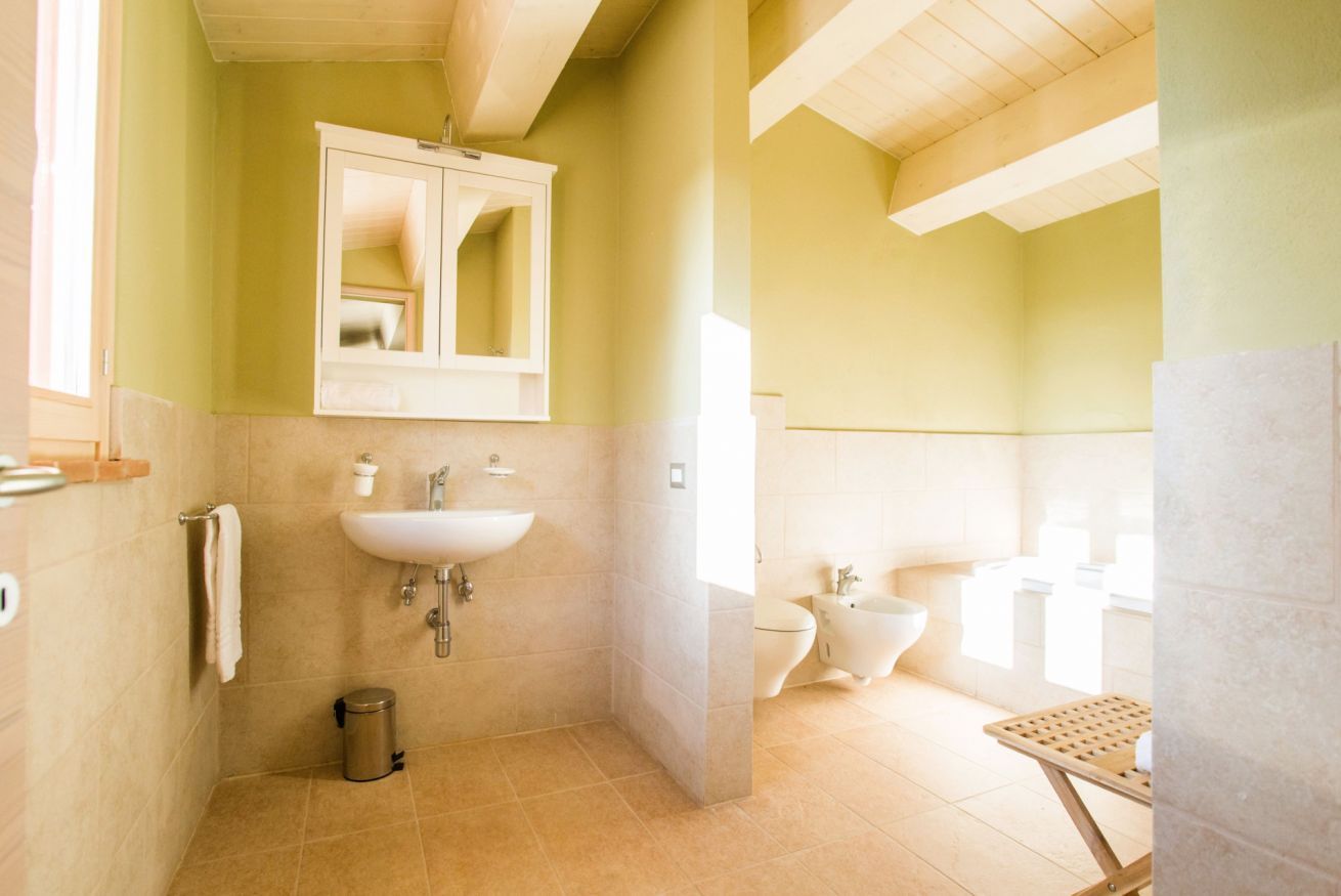 A bathroom with a sink, mirror, toilet, bidet, and a small trash bin.