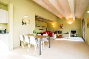 A spacious living area with a dining table, white chairs, a sofa, and a TV.