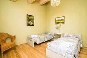 A bedroom with two beds, a wicker chair, and two framed pictures on the wall.