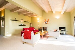 Una sala de estar con un sofá rojo, un sillón blanco y una televisión.