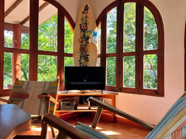 A room with a television, wooden furniture, and large windows with a view of trees. - OCEANFRONT PARADISE IN ROMANTIC NATURE - BAY VIEW - POOL - DIRECT BEACH ACCESS (San Juan del Sur)