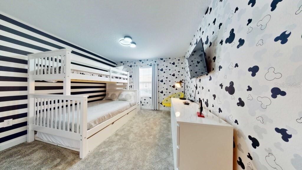 A child's bedroom with bunk beds, a desk, and a TV on the wall.