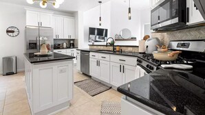 A modern kitchen with white cabinets, a black countertop, and stainless steel appliances. - Katy Oasis With Luxury Heated Pool & Game Room

 (Katy)