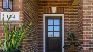 A brick building entrance with a door, a sign reading "1914", and a large potted plant. - Katy Oasis With Luxury Heated Pool & Game Room

 (Katy)
