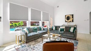 A spacious living room with a grey sectional sofa, a coffee table, and a view of a swimming pool. - Katy Oasis With Luxury Heated Pool & Game Room

 (Katy)