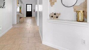 A spacious hallway with a high ceiling, a staircase, and a decorative wall with exposed brick and a mirror. - Katy Oasis With Luxury Heated Pool & Game Room

 (Katy)