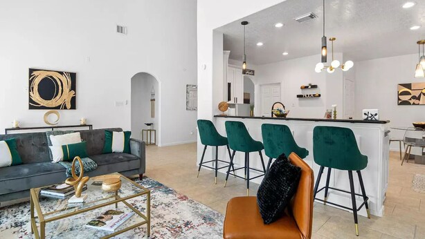 A modern living room with a sofa, coffee table, and a kitchen area with bar stools. - Katy Oasis With Luxury Heated Pool & Game Room

 (Katy)