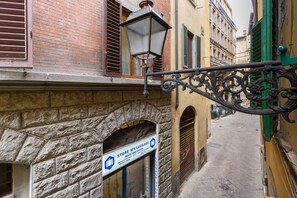 A narrow street with a stone archway, a storefront with a luggage storage sign, and a street lamp. - Madame Betta apartment in Florence by Mmega (Firenze)