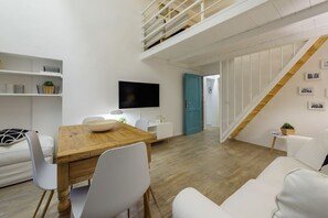 Een moderne woonkamer met een houten eettafel, witte stoelen, een flatscreen televisie, witte banken, een trap en een blauwe deur.