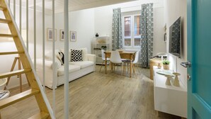 A modern living room with a white sofa, a wooden dining table, and a staircase. - Madame Betta apartment in Florence by Mmega (Firenze)