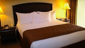 Une chambre d’hôtel avec un grand lit, une tête de lit sombre, deux tables de chevet avec des lampes et une petite table de nuit.