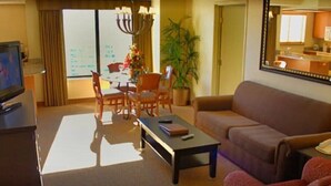 Un salon comprenant un canapé, une table basse, un téléviseur, une table à manger avec des chaises et une grande fenêtre.