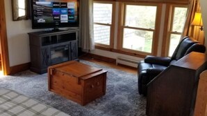 Een woonkamer met een televisie, een houten salontafel, een bank en een raam met jaloezieën.