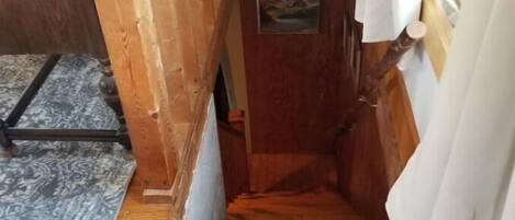 A narrow wooden staircase leading to a door with a small picture on it.