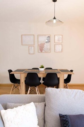 Un comedor con una mesa de madera, sillas negras, una lámpara colgante y cuadros en la pared.