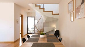 A modern dining area with a wooden table, black chairs, and a staircase in the background. - GuestReady - Charming Caniço Retreat (Santa Cruz)