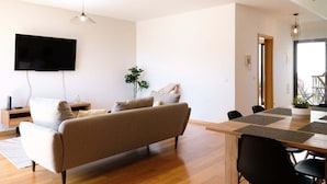 A modern living room with a sofa, a flat-screen TV, and a dining table with chairs. - GuestReady - Charming Caniço Retreat (Santa Cruz)