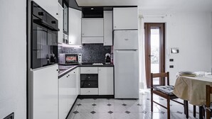 Cocina compacta con microondas, estufa y refrigerador, zona de comedor con mesa y sillas, y piso de baldosas.